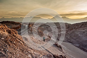 Young woman alone watching sunrise at Valle de la Luna Moon Valley, San Pedro de Atacama Chile. Wide view of stunning sun rise on