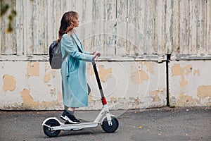 Young woman alternative commute with electric scooter in blue coat at the city