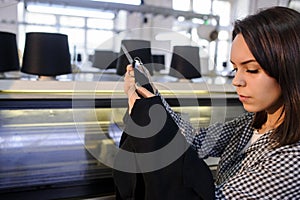 Young woman analyzing a knitted piece of cloths near industrial knitting machine with black cones on it
