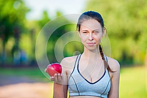 Young woman with apple and bottle of water after running outside. Female fitness model training outside in the park
