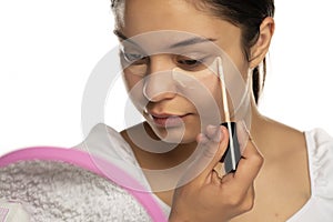 A young woman applies concealer under her eyes