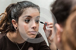 Young woman applies eyelash mascara in front of the mirror in the bathroom.