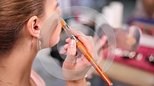 A young woman applies foundation to her face with a brush. Close-up