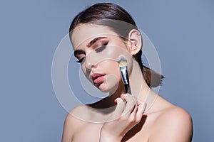 Young woman applies powder on the face using makeup brush. Beautiful girl doing contouring apply blush on cheeks. Face