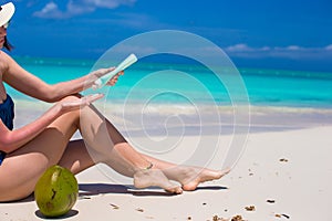 Young woman apply cream on her smooth tanned legs at tropical beach