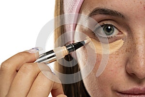 Young woman applyes concealer under her eyes