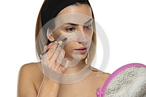 Young woman applyes concealer under her eyes on white