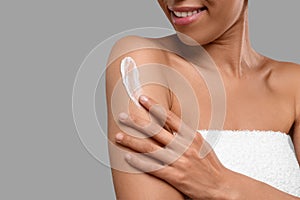Young woman applying body cream onto arm on grey background, closeup. Space for text