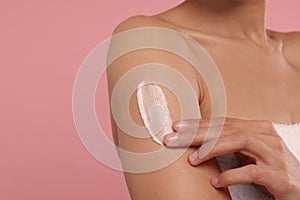 Young woman applying body cream onto arm on pink background, closeup. Space for text