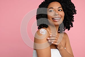 Young woman applying body cream onto shoulder on pink background. Space for text