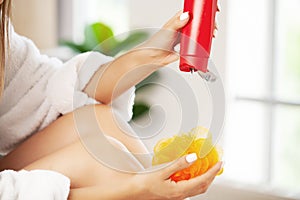 Young woman applying body lotion on legs