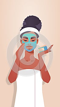 Young woman applying clay face mask dressed in towel african american girl skincare spa facial treatment concept