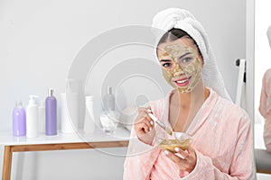 Young woman applying clay mask on her face in bathroom. Skin care