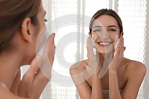 Young woman applying cleansing foam onto her face near mirror in bathroom