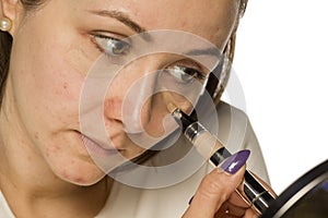 Young woman applying concealer on her face