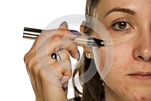 Young woman applying concealer on her face