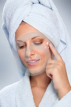 Young woman applying cosmetic cream on a clean fresh face