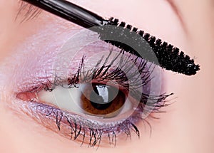 Young woman applying cosmetics on eyelashes