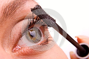 Young woman applying cosmetics on eyelashes macro
