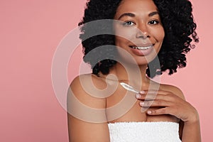 Young woman applying cream onto body on pink background. Space for text