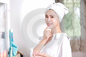 Young woman applying cream to face mirror reflection at dressing