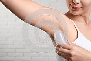 Young woman applying crystal  deodorant to armpit against brick wall, closeup