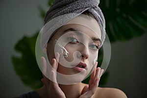 Young woman applying face cream on her face