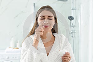 Young woman applying face cream onto her nose in bathroom