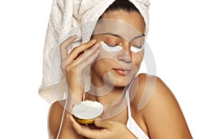 Young woman applying face cream under her eyes