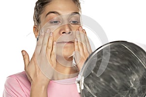 Young woman applying face cream on white