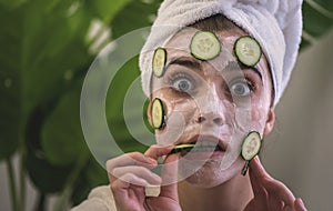 Young woman applying face mask with cucumbers on her face