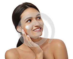 Young woman applying facial cream on white background