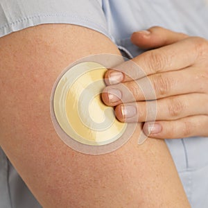 YOUNG WOMAN APPLYING FLESH COLOURED NICOTINE PATCH TO ARM