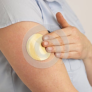 YOUNG WOMAN APPLYING FLESH COLOURED NICOTINE PATCH TO ARM