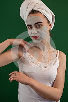 young woman applying green clay mask isolated on green