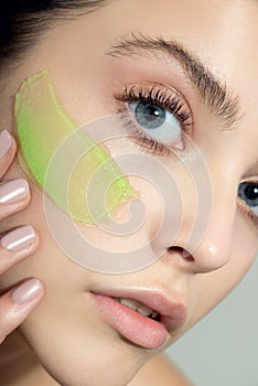 Young woman applying green gel face cream or facial mask at her face. Beauty model with perfect fresh skin and long eyelashes