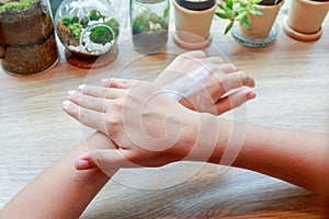 Young woman applying hands moisturizer lotion on wooden table