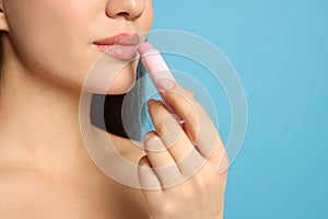 Young woman applying lip balm on turquoise background, closeup. Space for text