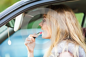 Young woman applying lipstick in car