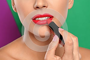 Young woman applying lipstick on color background