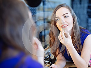 Young woman applying lipstick in front of a mirror