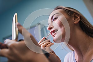 Young woman applying lipstick looking at mirror