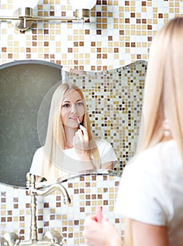 Young woman applying lipstick looking at mirror