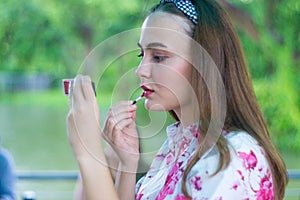 Young woman applying lipstick looking at mirror