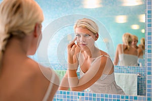 Young woman applying lotion on face at home