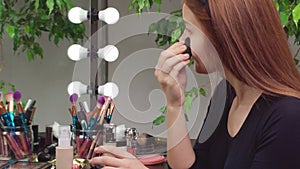 Young woman applying make-up while sitting at her vanity table with lots of cosmetics