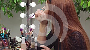 Young woman applying make-up while sitting at her vanity table with lots of cosmetics