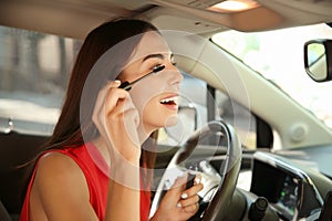 Young woman applying makeup on driver's seat of car