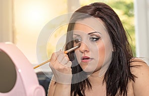 Young woman applying makeup on her face, light effect