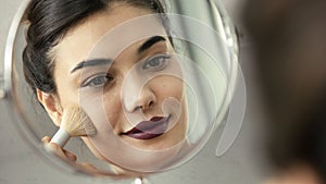 Young woman applying makeup to her face with a brush